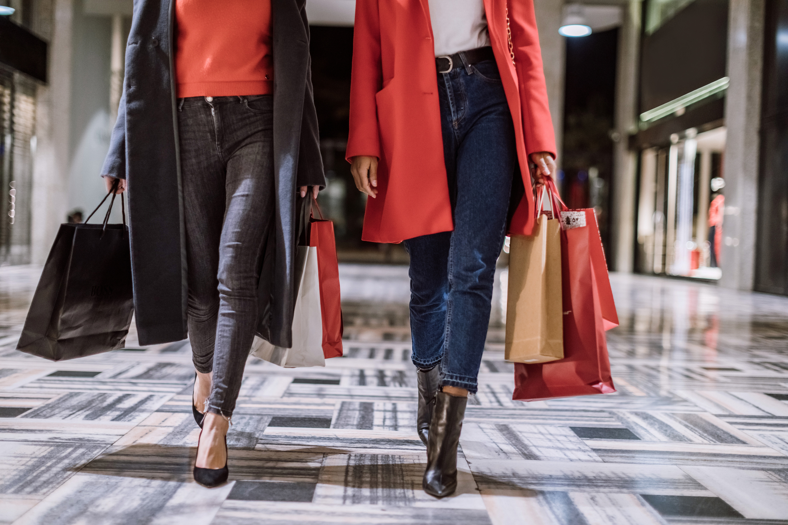 two individuals walking through a mall with shopping bags enjoying a personal shopping experience