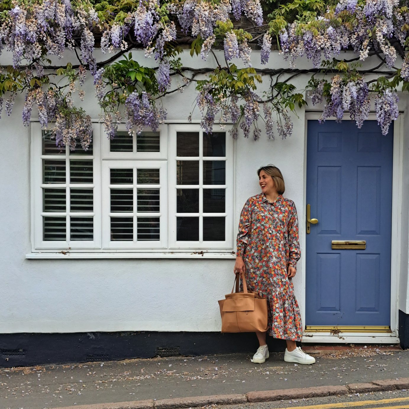 Personal stylist, Katie Jane in a floral dress stands confidently smiling in front of a blue door