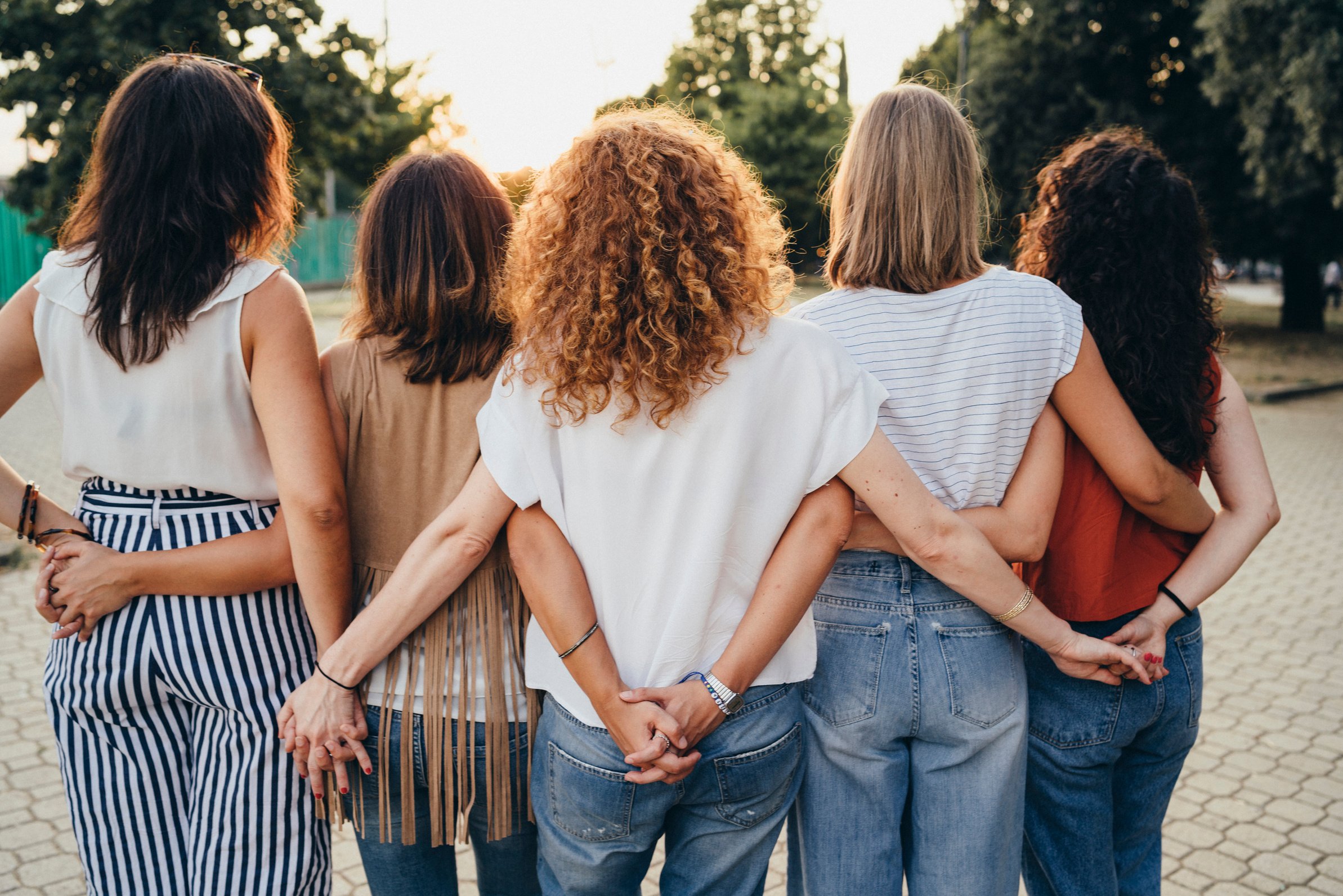 back view of a group of individuals holding hands in a park at sunset. Friends enjoying a style party together