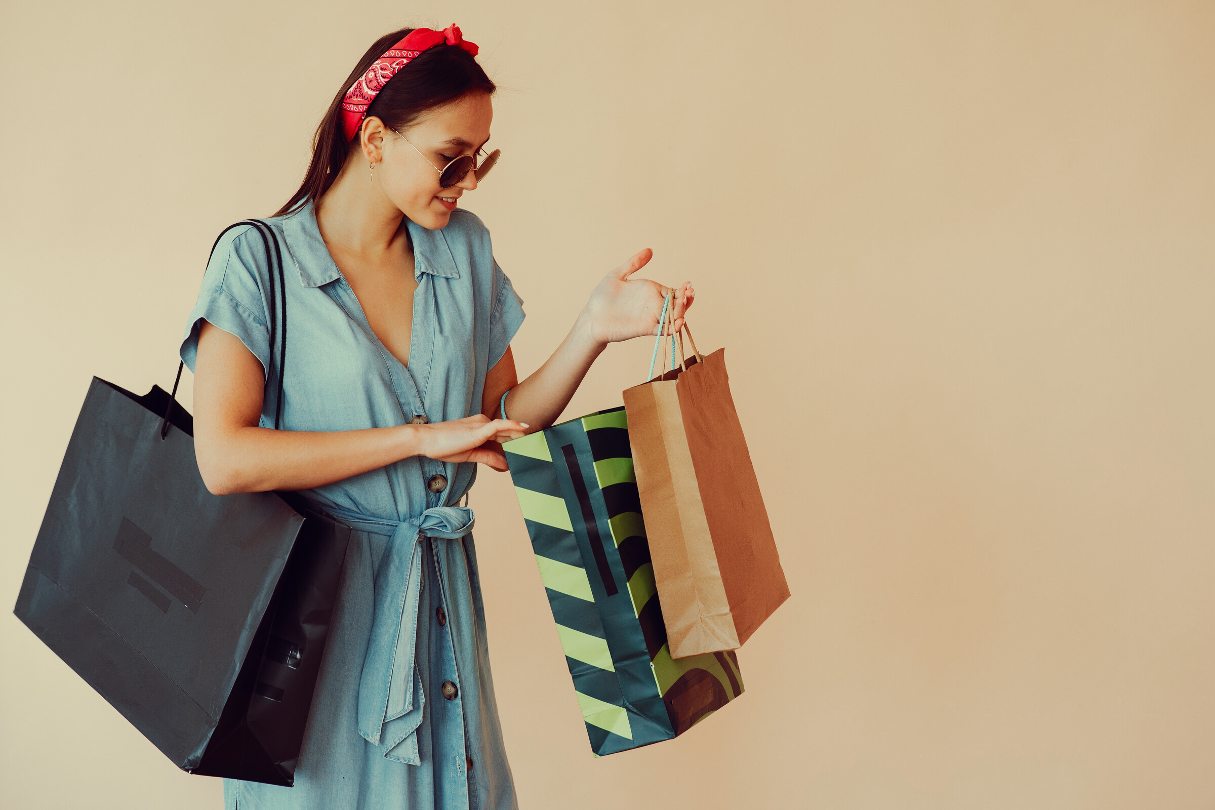 Happy young lady with shopping bags on beige background